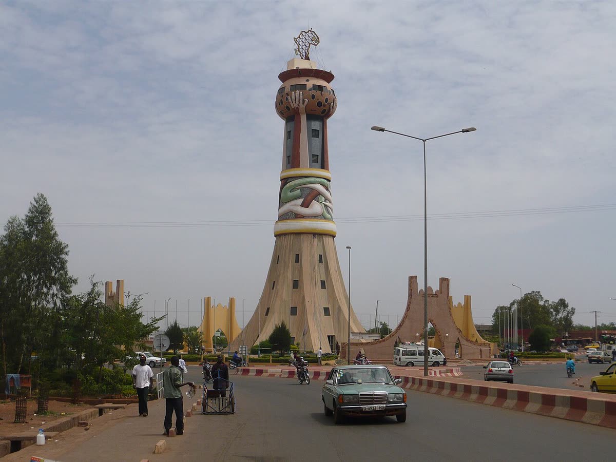 The Tour d'Afrique in Bamako, with a taxi and people walking on the road in front of it.